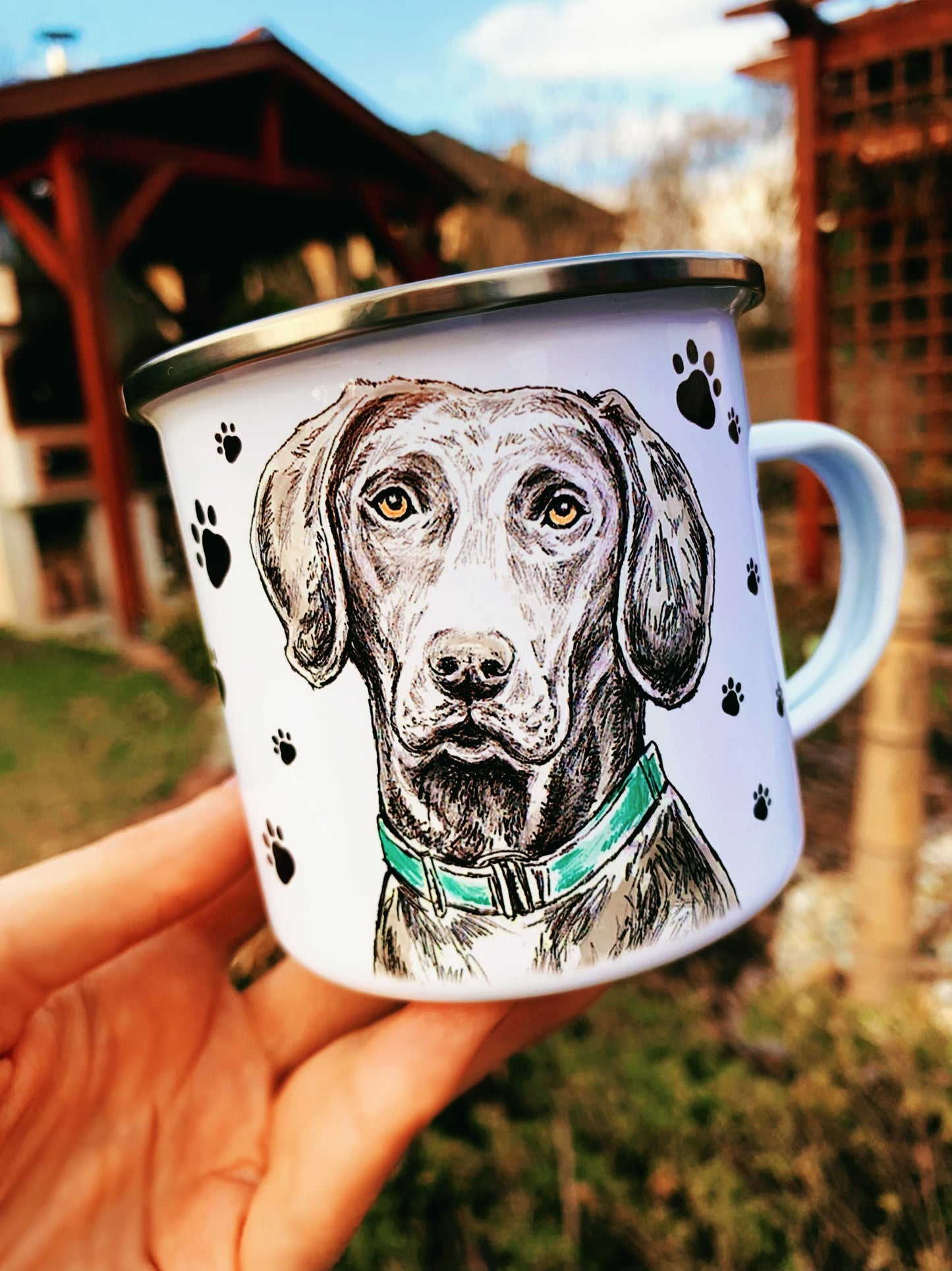 Részletgazdag kézzel festett weimari vizsla portré fém bögrén, hátterében apró fekete mancsnyomokkal.