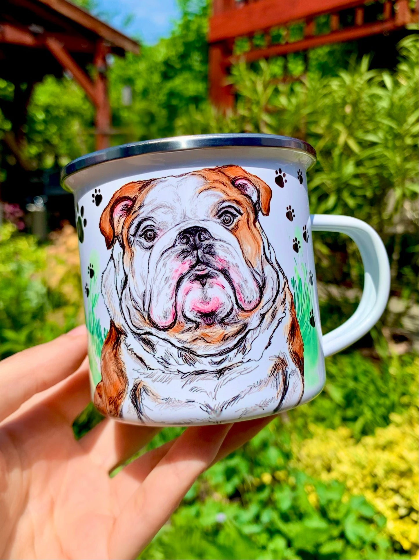 Ülő angol bulldog fém bögrén, fűben ülve, mancs mintás háttérrel