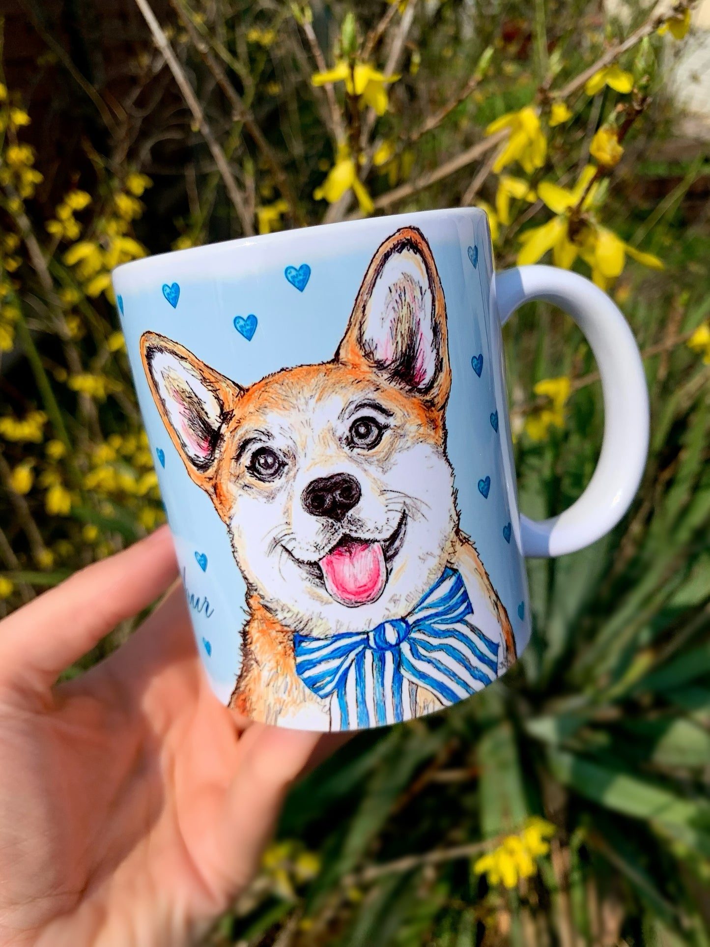 Kerámia bögre mosolygó Corgi kutyával és világoskék apró szív mintás háttérrel, kézzel rajzolt és festett részletekkel, fehér alapon.