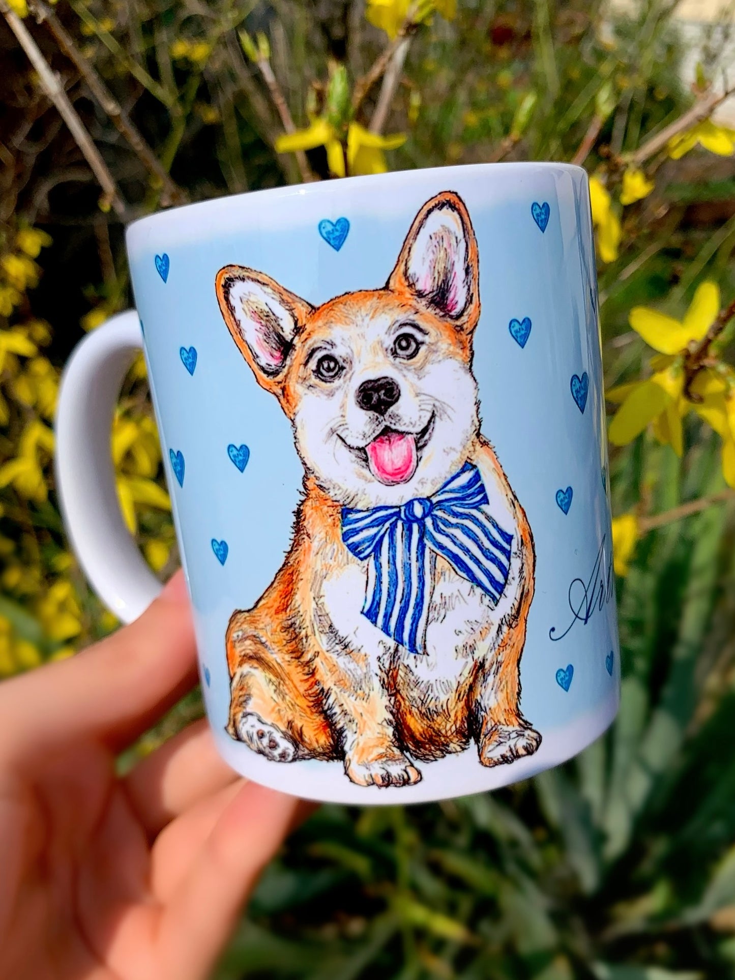 Mosolygó, világosbarna-fehér Corgi illusztrációval díszített kerámia bögre, kézzel festett világoskék apró szív mintákkal, fehér háttérrel.