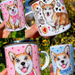 Corgi kutyás ajándékkollekció – kézzel festett mintás bögrék, kulacs és vászontáska világosbarna-fehér kutyával, rózsaszín szívekkel, fehér háttérrel.