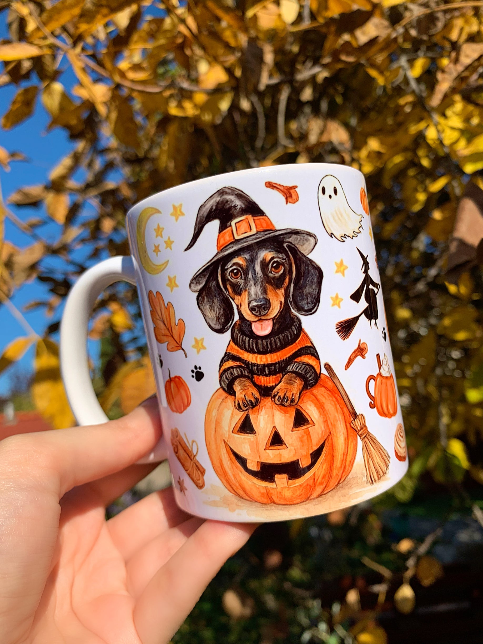 Kézzel festett cser színű tacskó mintás kerámia bögre boszorkánykalappal és halloweeni tökös, szellemes, fahéjas csigás motívumokkal, prémium iparművészeti ajándék tacskórajongóknak.