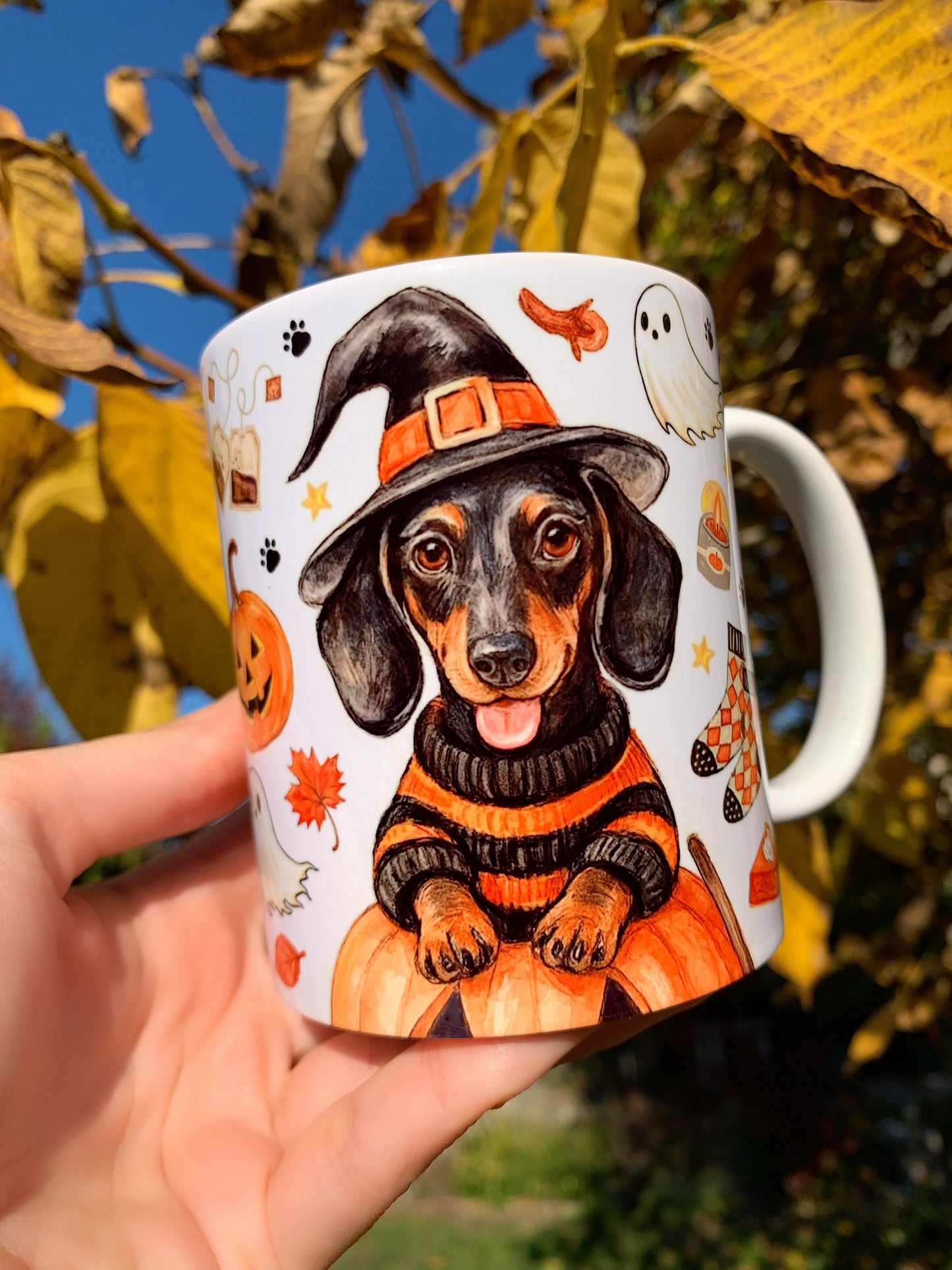 Egyedi, kézzel rajzolt és akvarellel festett tacskós bögre halloweeni hangulatban, boszorkánykalapos tacskóval, sütőtökökkel és őszi motívumokkal díszítve, prémium minőségű iparművészeti ajándék.