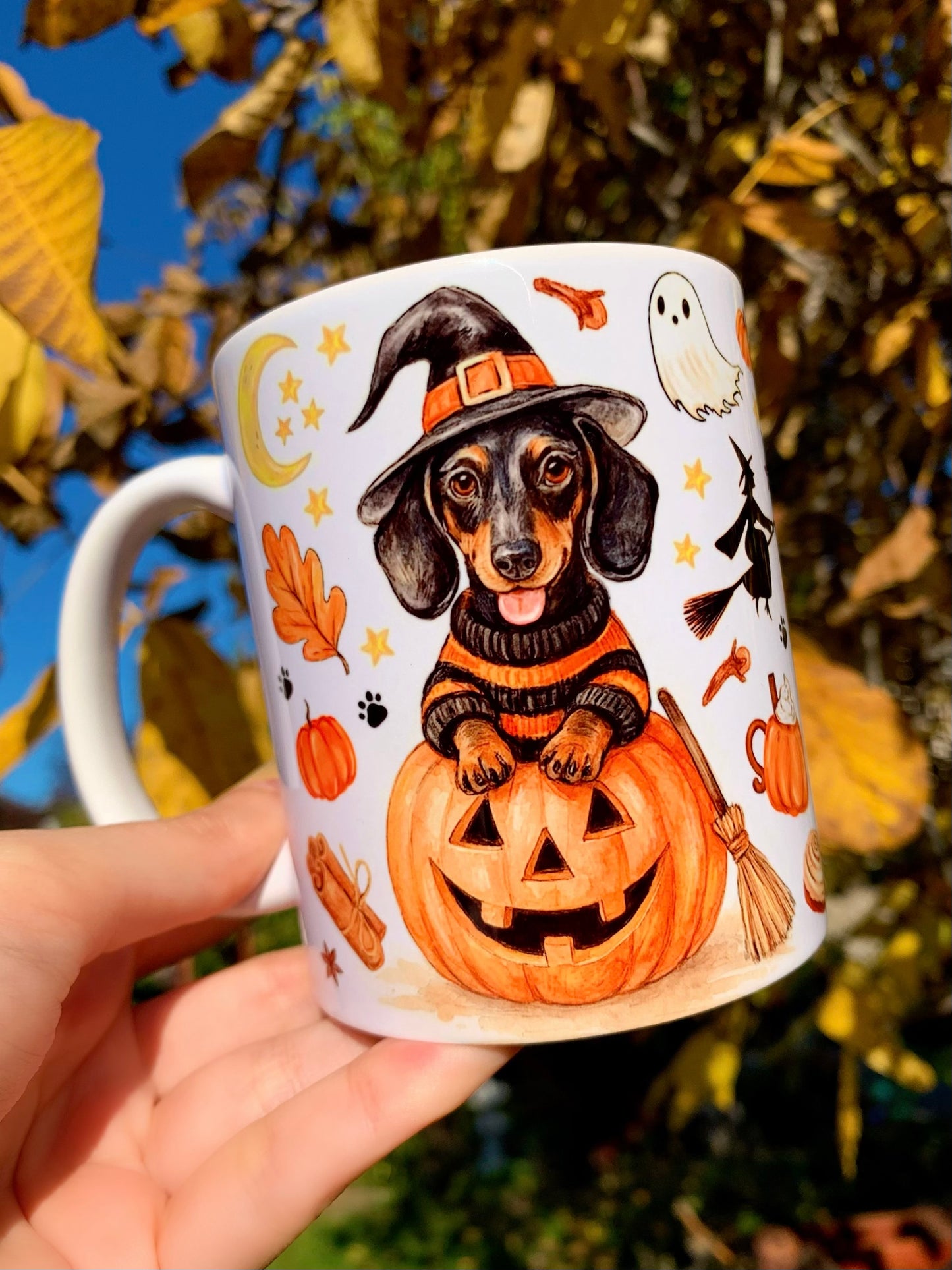 Kézzel rajzolt és akvarellel festett halloweeni tacskós bögre, iparművészeti részletességgel megalkotott cser tacskóval, boszorkánykalappal és őszi sütőtök motívumokkal.