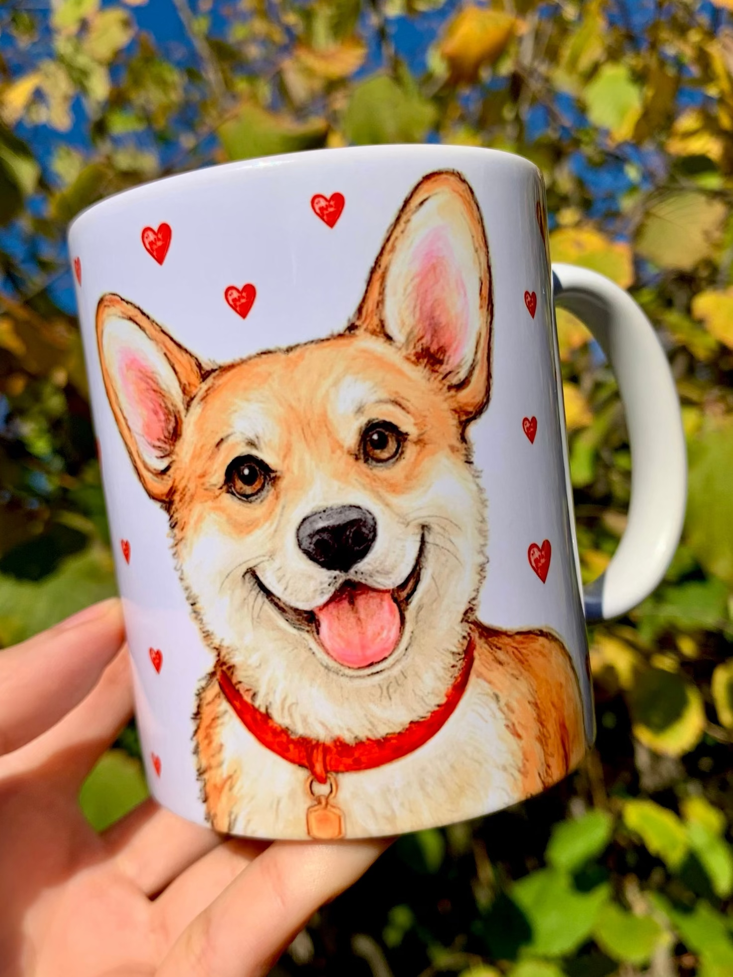 Kézzel festett Corgi kutyás bögre, amelyen Pusztai Juci iparművész egyedi, akvarellhatású illusztrációja látható. A mosolygó világosbarna-fehér Corgi mellett apró piros szívecskék díszítik a bögrét, romantikus, szeretetteljes hangulatot teremtve – tökéletes kézműves ajándék Corgi gazdiknak és kutyabarátoknak. ❤️☕🐶