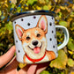 Kézműves Corgi kutyás bögre, amely akvarellfestékkel megrajzolt, mosolygó Corgit ábrázol. A piros nyakörves kutyus részletgazdagan kidolgozott, a háttér mintázata választható – szívecskés vagy mancsos. Ideális ajándék Corgi gazdiknak és kutyabarát kávérajongóknak.