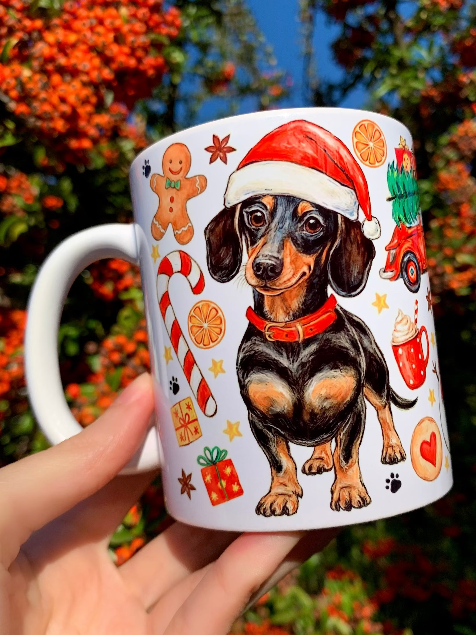 Tacskós bögre karácsonyi mintákkal. Karácsonyi kerámia bögre kézzel festett tacskó illusztrációval és piros nyakörvvel. A minta részletes akvarell árnyalatokat és ünnepi motívumokat tartalmaz. Stílusos, kézműves hatású ünnepi ajándék