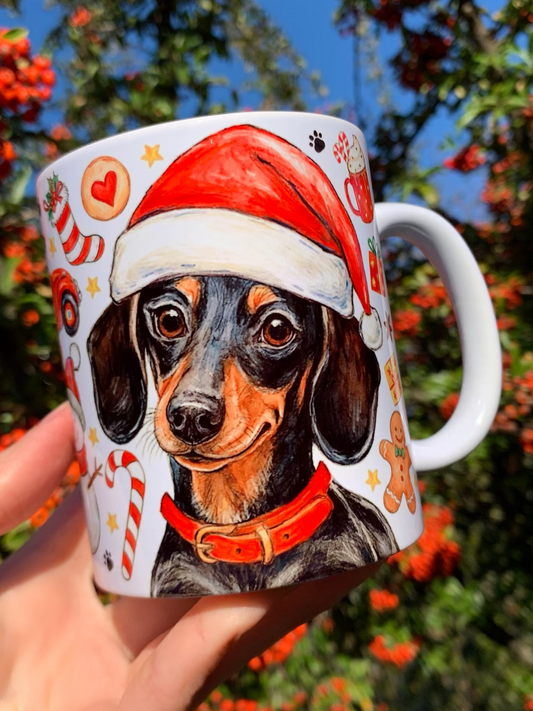 Prémium minőségű karácsonyi kerámia bögre kézzel rajzolt és akvarellel festett cser színű tacskóval, piros nyakörvvel és ünnepi motívumokkal. A részletgazdag kutyailusztráció köré mézeskalács figurák, piros–fehér cukorkák, arany harangok és zöld fenyőágak kerültek, finom akvarellárnyalatokkal. A kézműves stílusú minta meleg, ünnepi hangulatot teremt, tökéletes ajándékká téve a bögrét karácsonyra.