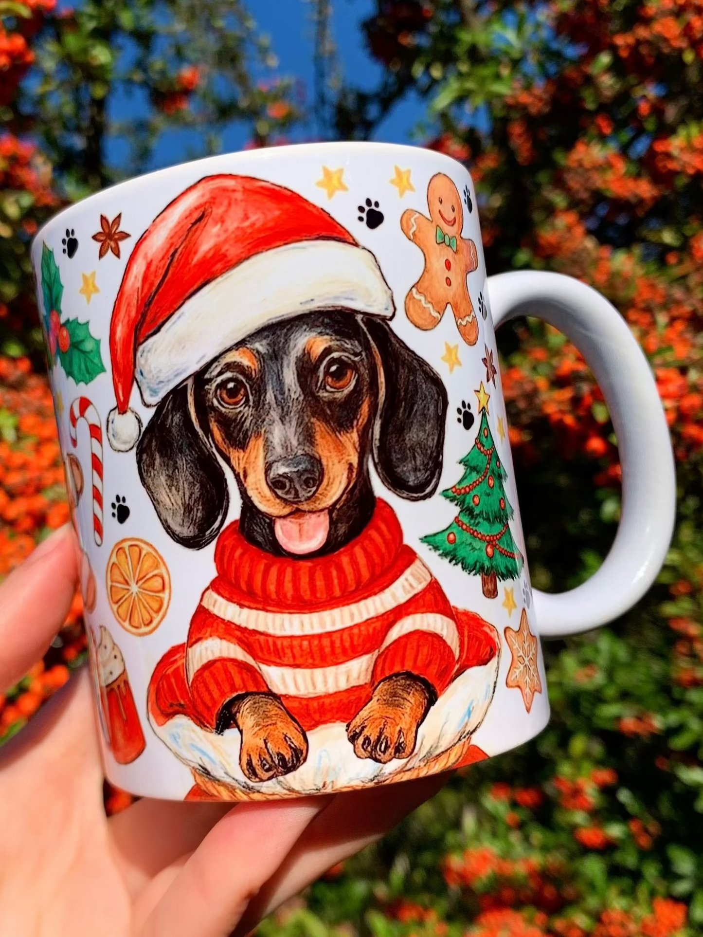 Karácsonyi tacskós bögre prémium kézzel festett mintákkal. Prémium minőségű karácsonyi kerámia bögre kézzel rajzolt, finoman árnyékolt ceruzavonalas és akvarellel festett tacskó illusztrációval. A kutya kedves, bájos, ünnepi hangulatú pózban jelenik meg, vörös–zöld karácsonyi dekorokkal és meleg, természetes akvarellszínekkel.