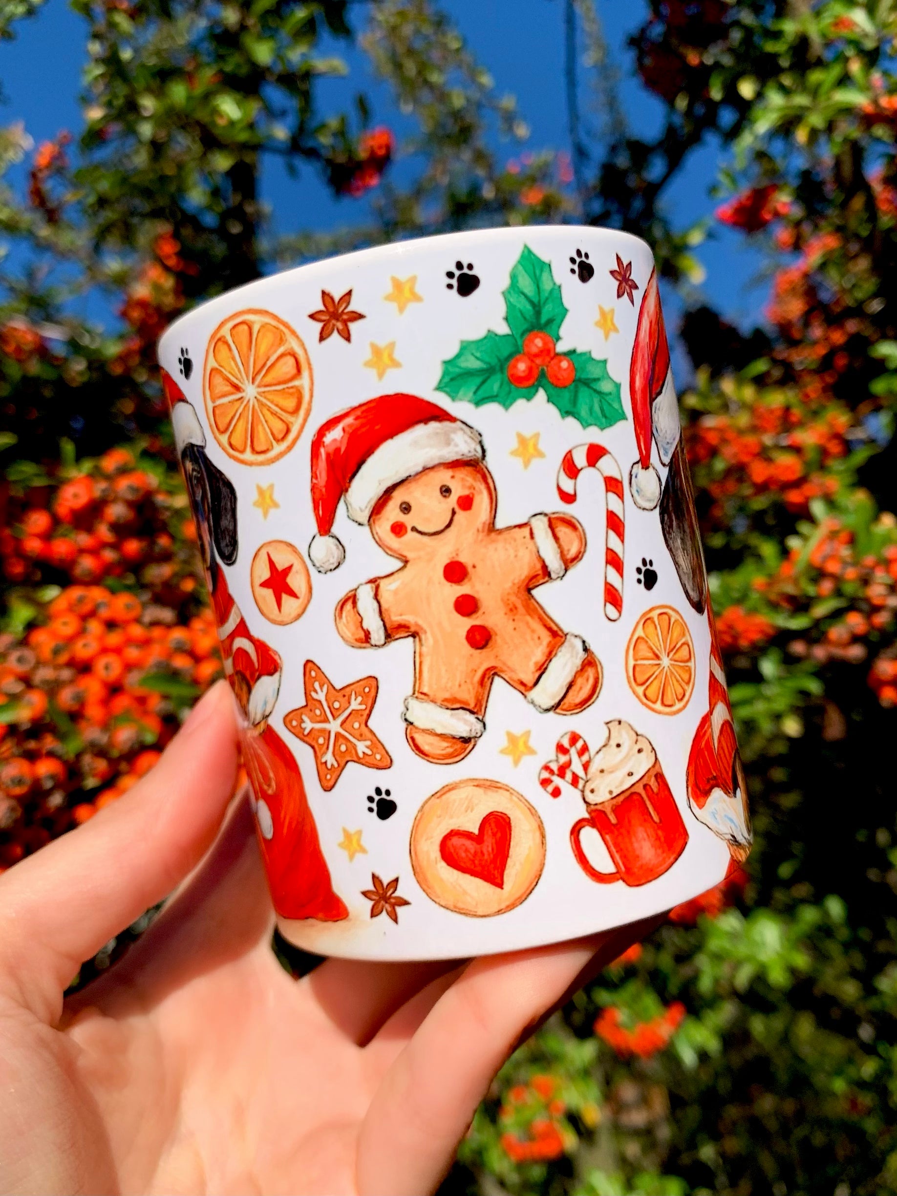 Karácsonyi hangulatú kerámia bögre kézzel rajzolt, akvarellel festett tacskó illusztrációval. A kutya bájos, szerethető tekintettel néz, körülötte vörös és zöld ünnepi motívumokkal. Kézműves, festett hatású design