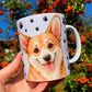 Kézzel rajzolt Corgi illusztrációval díszített bögre, akvarell részletekkel és mancs mintás háttérrel. A Corgi portré kedves tekintettel néz ránk, a másik oldalon álló kutya látható. Prémium tacskós ajándék kutyarajongóknak.