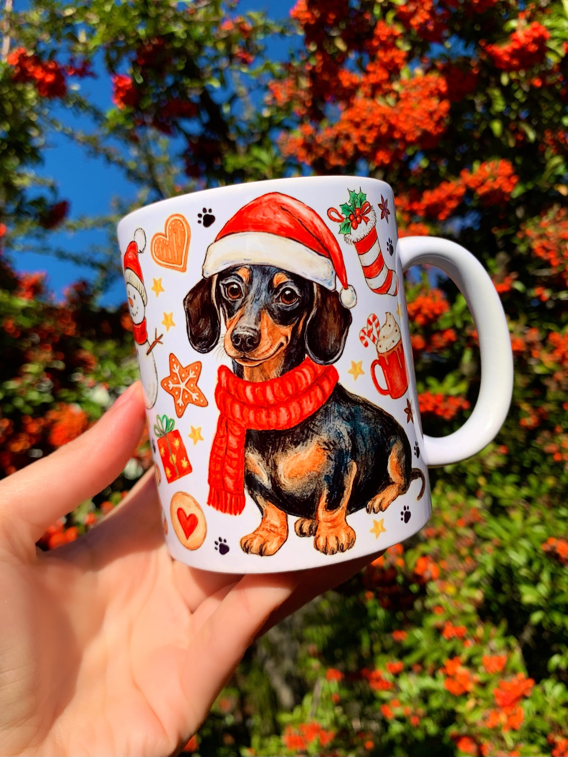 Ünnepi hangulatú tacskós kerámia bögre részletgazdag, kézzel rajzolt tacskó portréval és karácsonyi elemekkel. Cser tacskó mikulássapkában, szerethető, bájos grafikával. Ideális ajándék kutyabarátoknak karácsonyra.