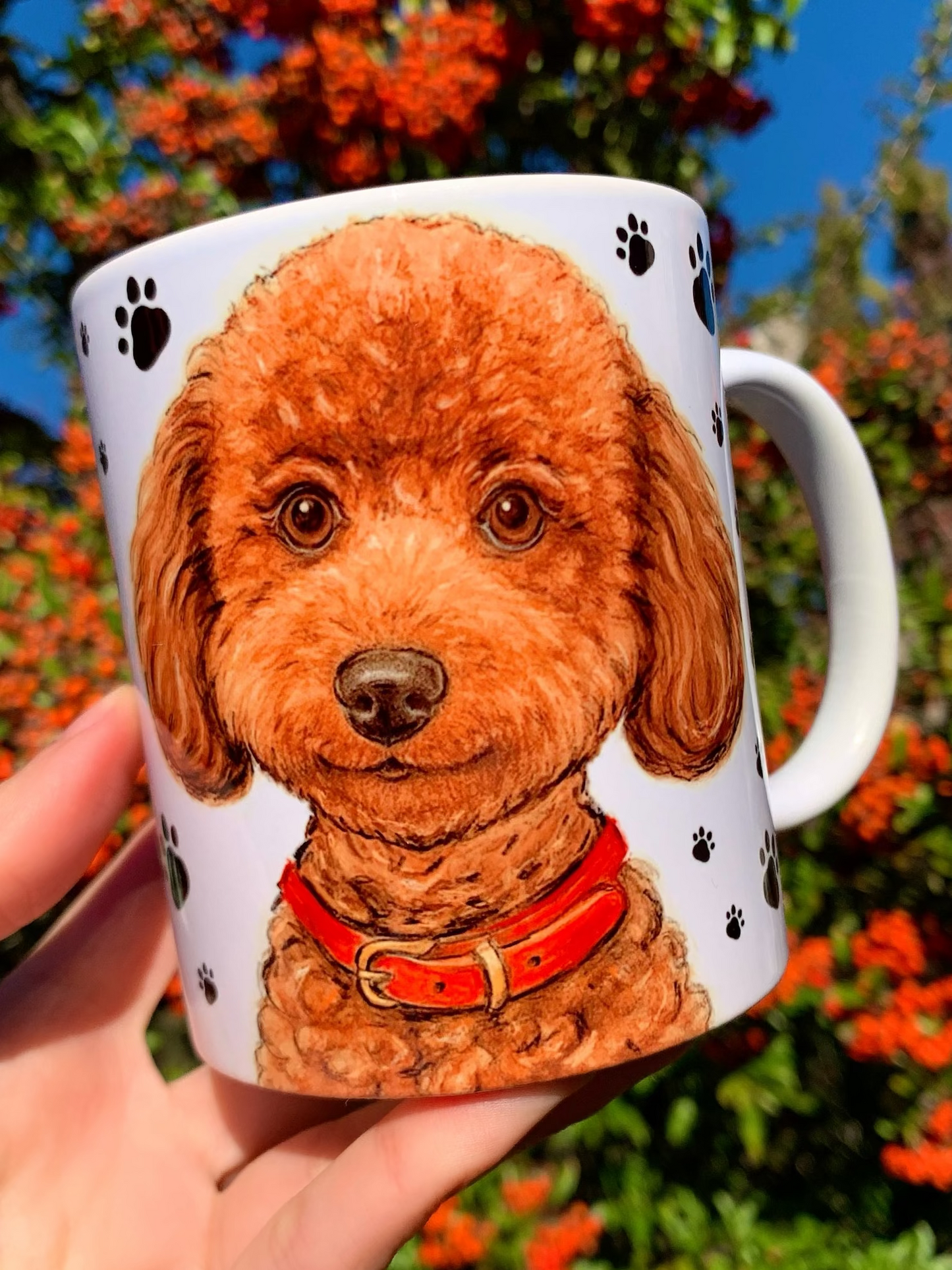 Kézzel festett Toy Poodle kerámia bögre fekete mancsos háttérrel, Pusztai Juci iparművész eredeti, kézzel rajzolt barna, göndör szőrű toy uszkár portréjával. A bögre egyik oldalán részletgazdag, mosolygó uszkár fej látható piros nyakörvvel, a másik oldalon az egész alakos, ülő Toy Poodle illusztráció szerepel. Magyar kézműves prémium kutyás ajándék gazdiknak, kutyabarátoknak, elegáns fekete-fehér mancs mintával és akvarellhatású kutyaportréval.