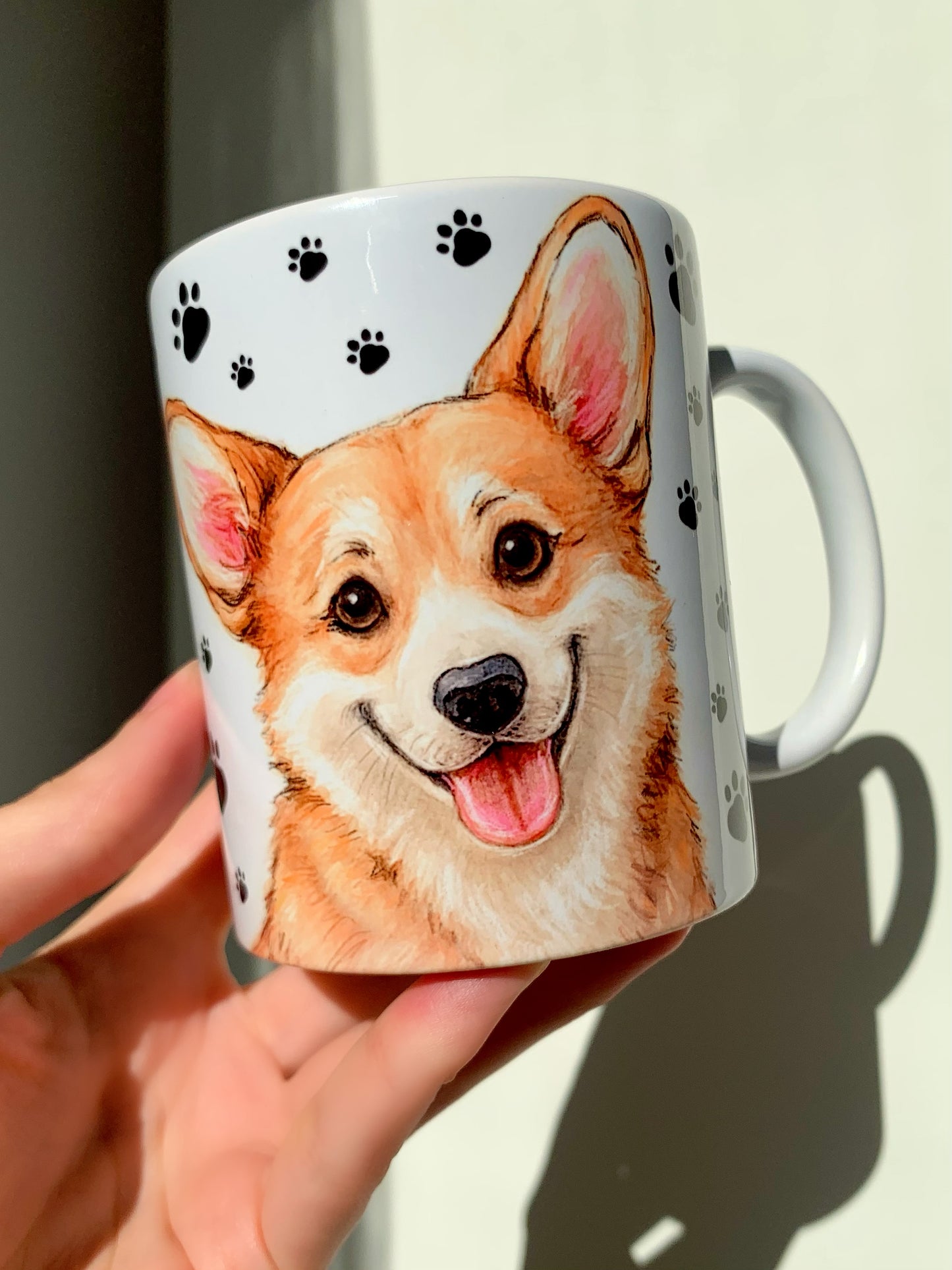 Egyedi kézműves Corgi kutyás bögre, részletgazdag portréval és teljes alakos illusztrációval. A kutyus körül apró, kézzel rajzolt mancs minták láthatók. Tökéletes reggeli kávés vagy teázós kiegészítő gazdiknak.