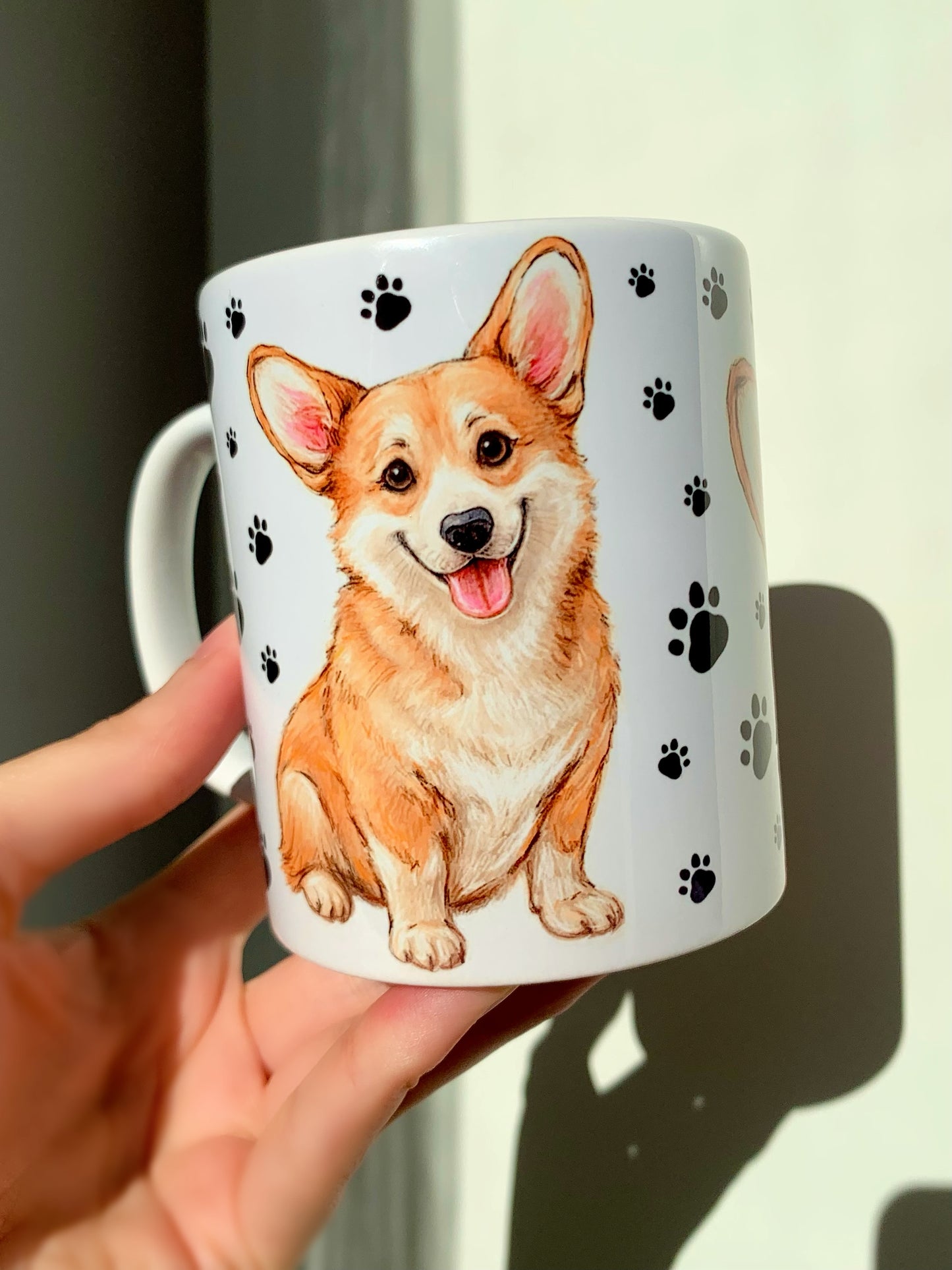 Corgi kutyás kerámia bögre kézzel festett illusztrációval, amely a fajta barátságos, játékos karakterét ragadja meg. Mancsos háttér és kétféle Corgi minta díszíti, ideális ajándék kutyabarátoknak.