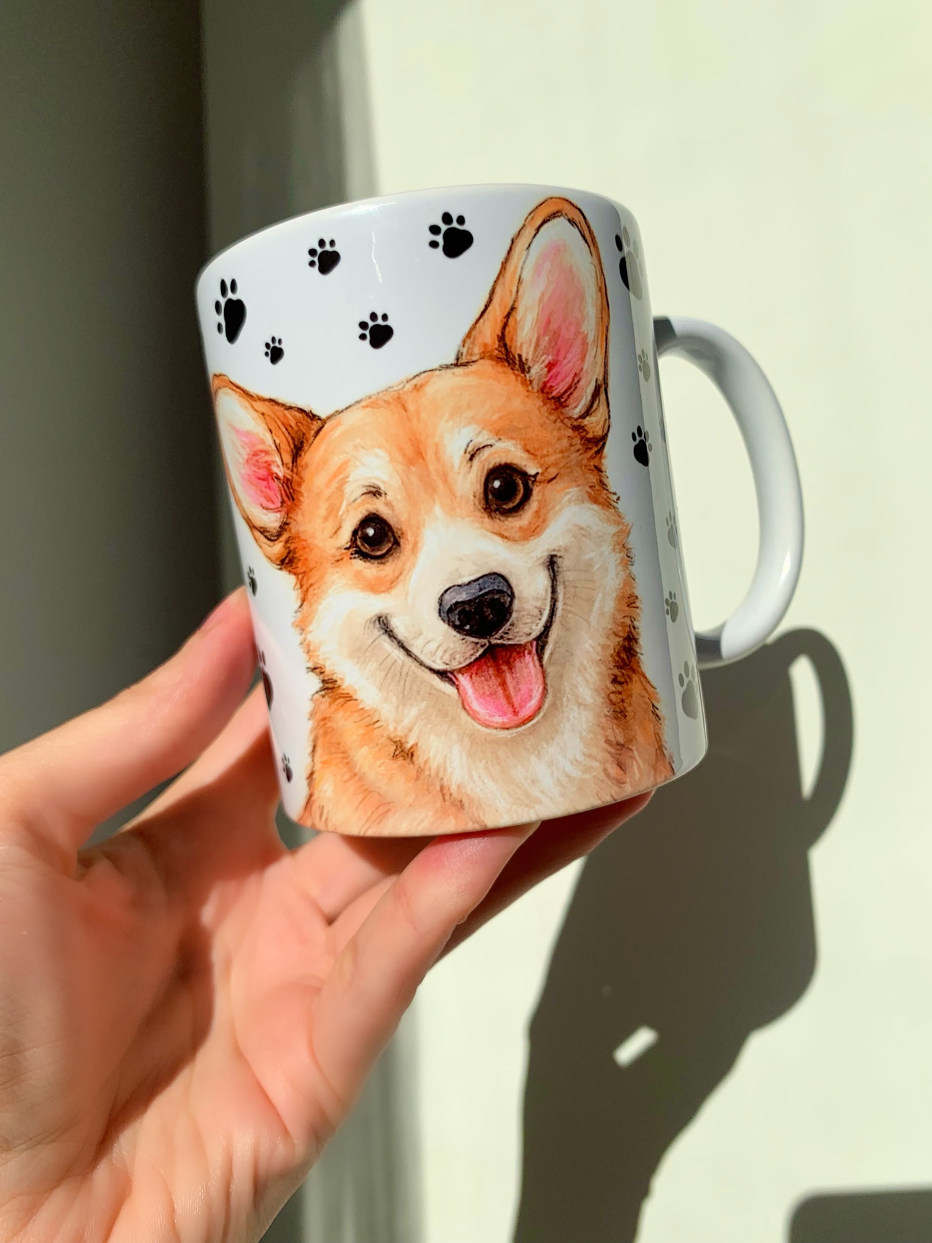 Prémium minőségű Corgi kutyás ajándék bögre, kézzel festett illusztrációkkal, mancs mintás háttérrel. A bögrét mosolygó Corgi portré és kedvesen álló kutyus díszíti, ideális minden Corgi gazdinak.
