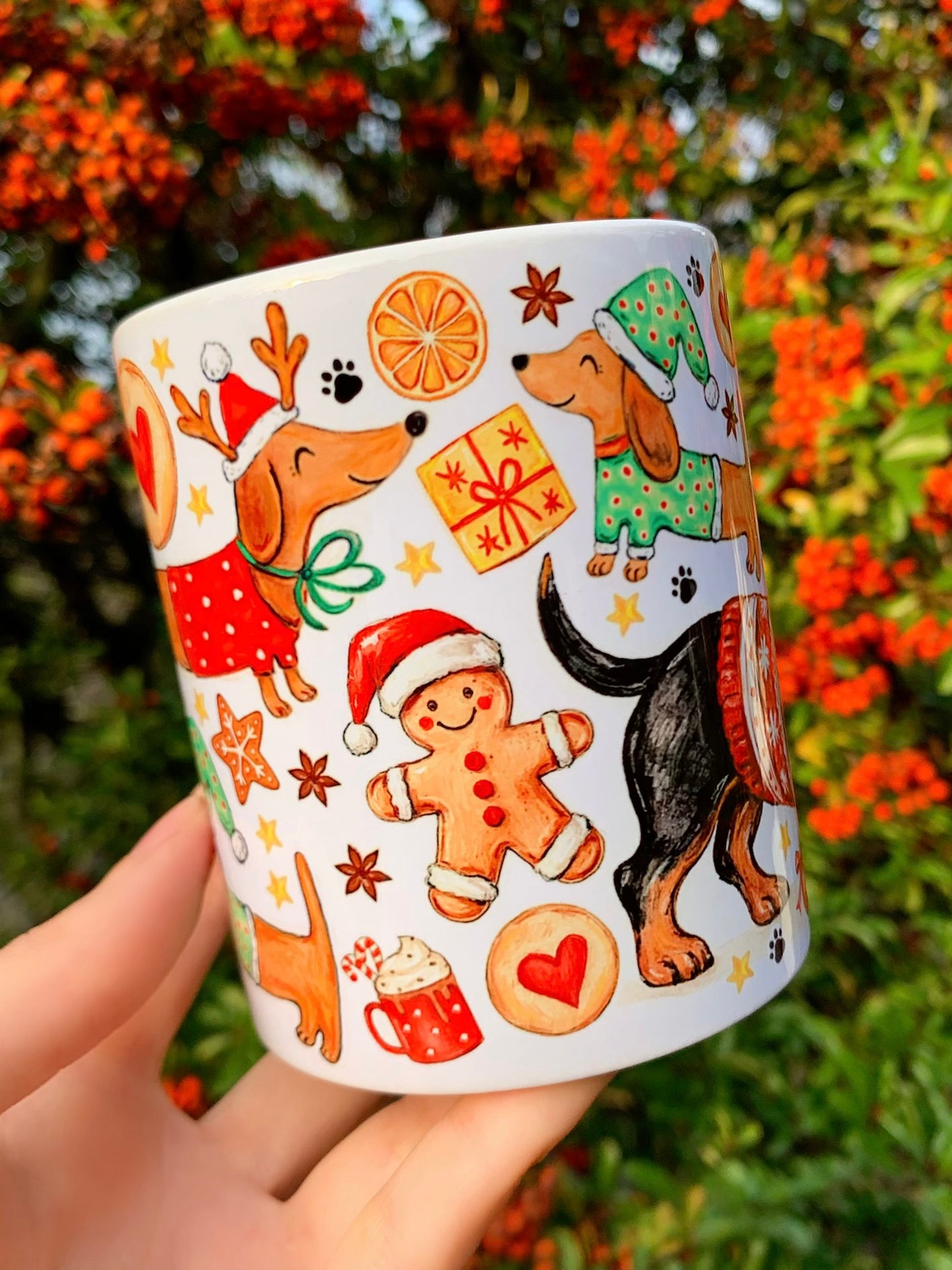 Kézzel rajzolt tacskós karácsonyi illusztráció bögrén. Akvarell technikával festett mézeskalácsok és ünnepi motívumok díszítik. Prémium kutyás bögre karácsonyi használatra.