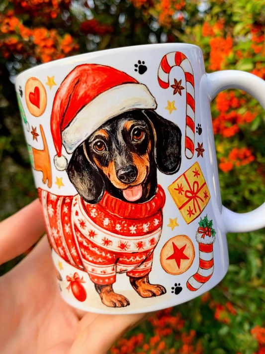 Karácsonyi tacskós bögre kézzel festett akvarell tacskó mintával. Álló tacskó piros karácsonyi pulcsiban, körülötte sok apró tacskó Mikulás-sapkában, mézeskalács figurákkal és ünnepi karácsonyi díszekkel. Prémium tacskós ajándék gazdiknak, egyedi kézműves kutyás bögre karácsonyra, iparművészeti illusztrációval.