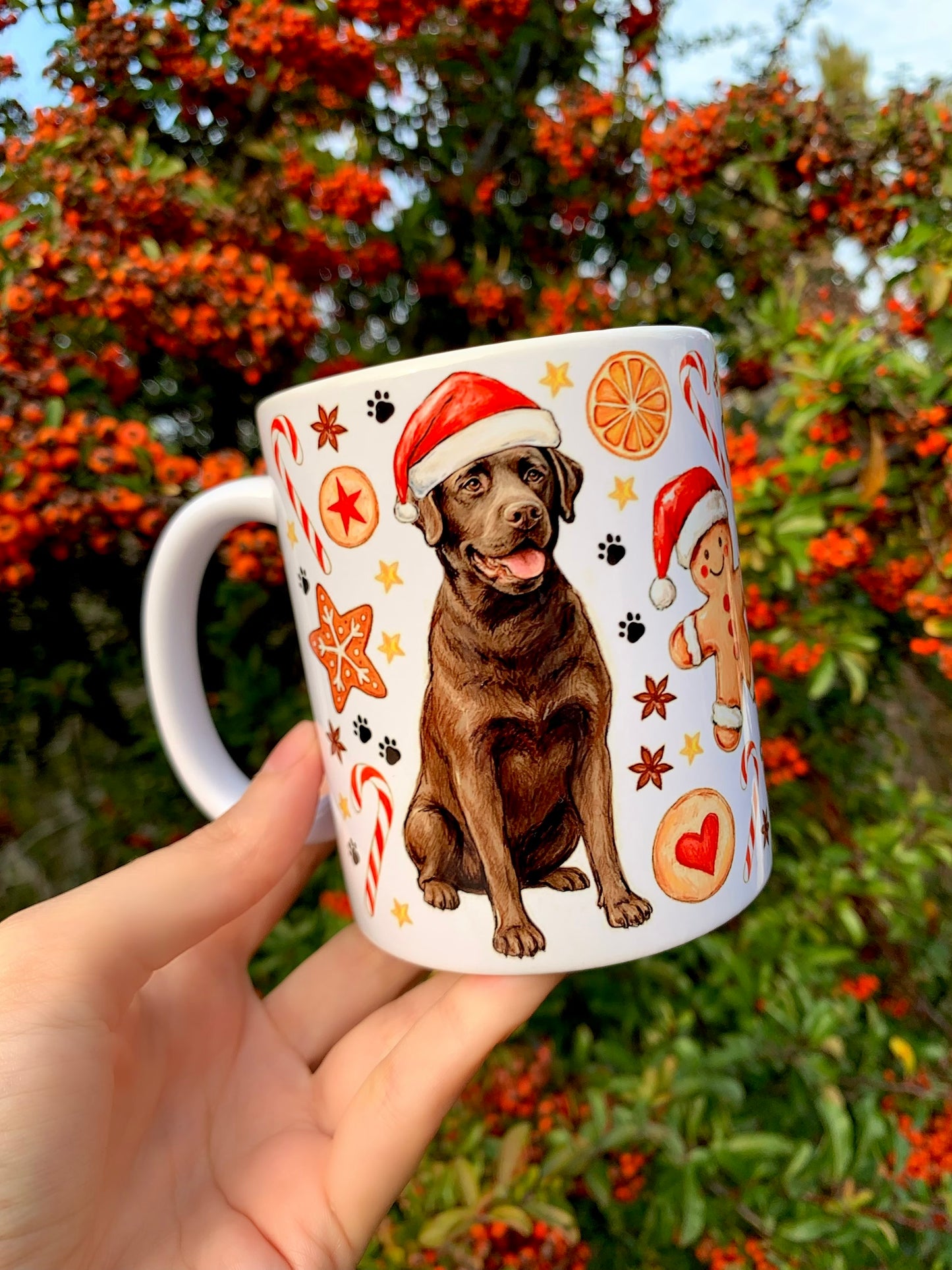 Karácsonyi labradoros bögre részlet, grafitceruzás körvonalakkal és akvarell színezéssel. Mikulás-sapkás labrador és mézeskalács motívumok díszítik. Egyedi kutyás ajándék bögre.