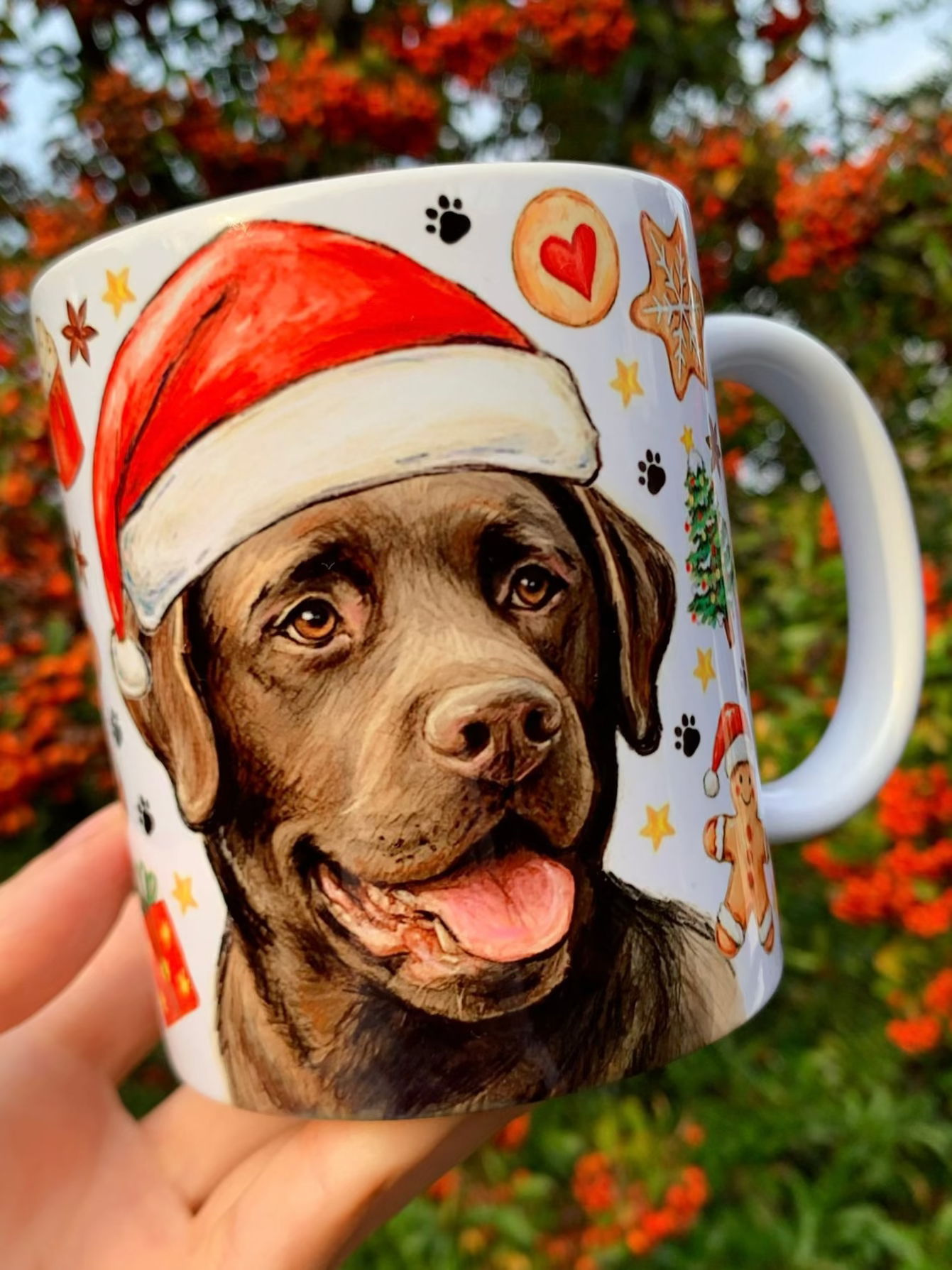 Karácsonyi labrador kutyás kerámia bögre kézzel festett labrador kutya mintával. A bögrén Sötétbarna labrador ül ünnepi pózban, Mikulás-sapkában, körülötte mézeskalács figurák, karácsonyi díszek és piros–zöld ünnepi motívumok. Prémium labradoros ajándék gazdiknak, egyedi kézműves kutyás bögre karácsonyra.