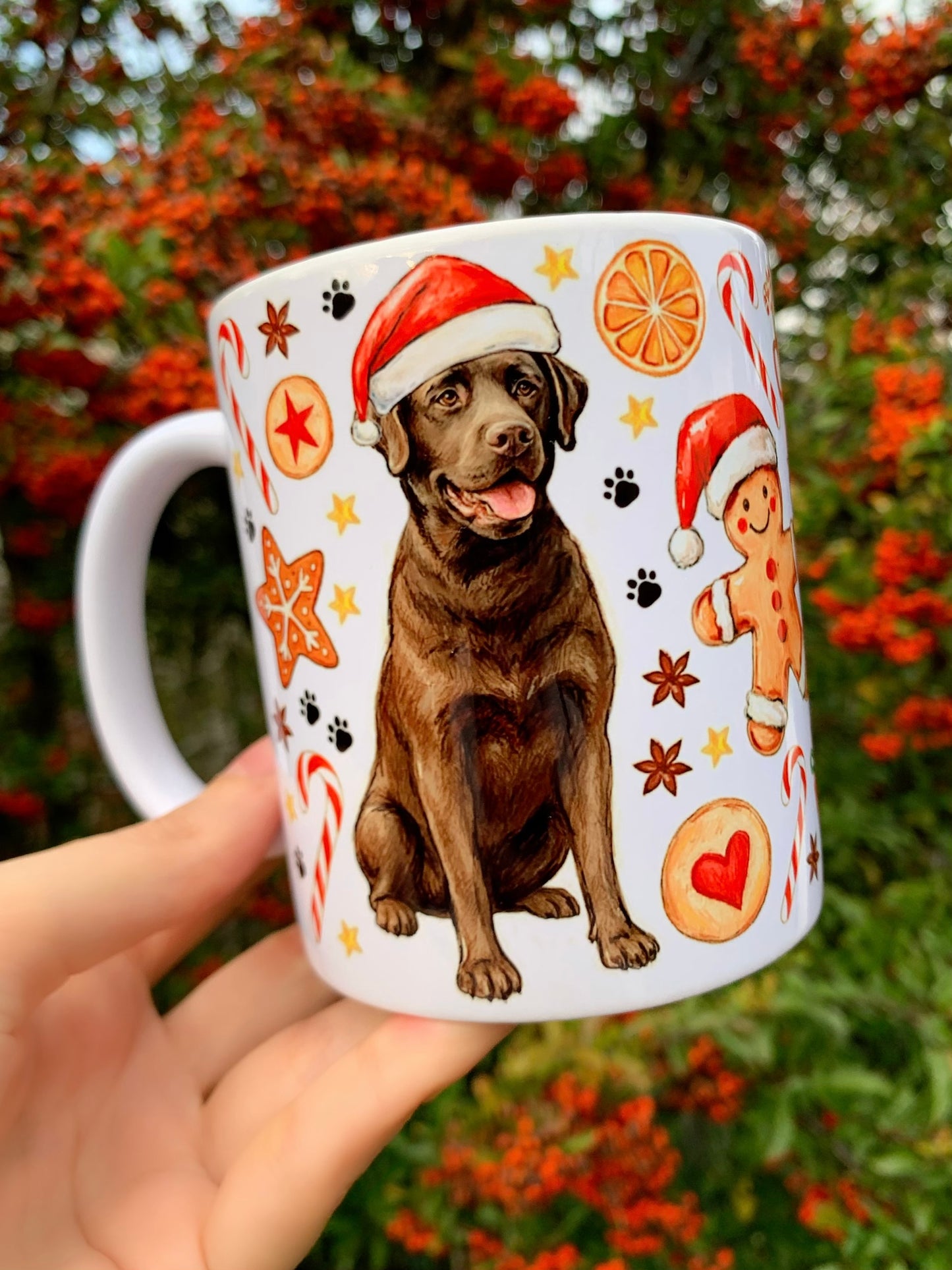 Kézzel rajzolt barna labrador karácsonyi minta bögrén, akvarell festéssel és látható grafitceruza vonalakkal. A mintán téli öltözetes labrador, Mikulás-sapka, mézeskalácsok és ünnepi dekorációk láthatók. Karácsonyi labrador bögre különleges kutyás ajándéknak.