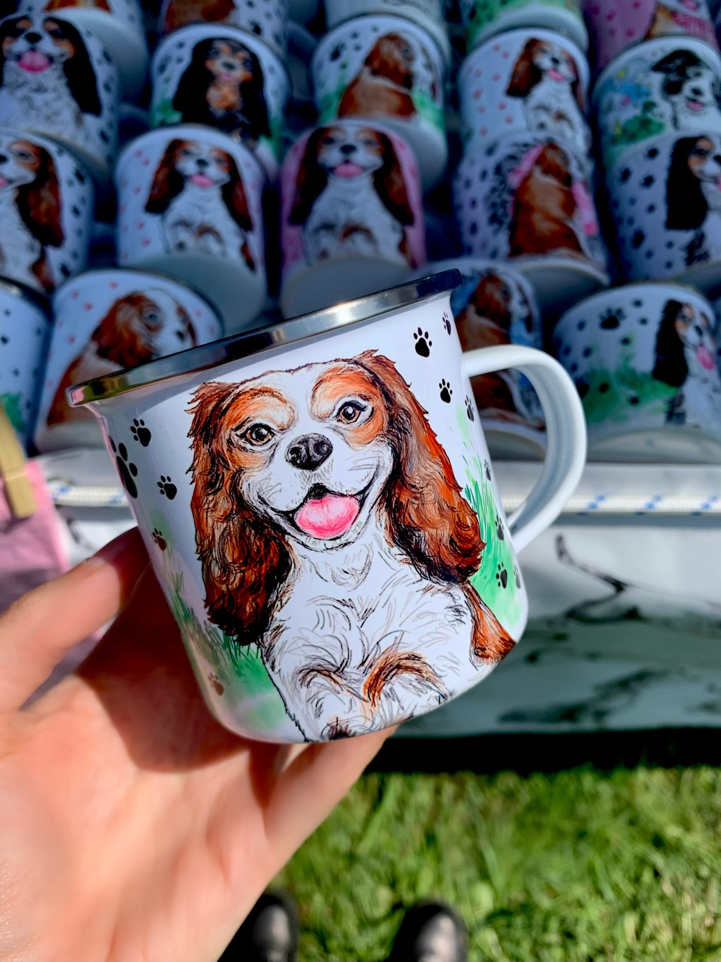 Vidám Cavalier spániel illusztráció fém bögrén fekete mancs mintákkal és zöld füves háttérrel