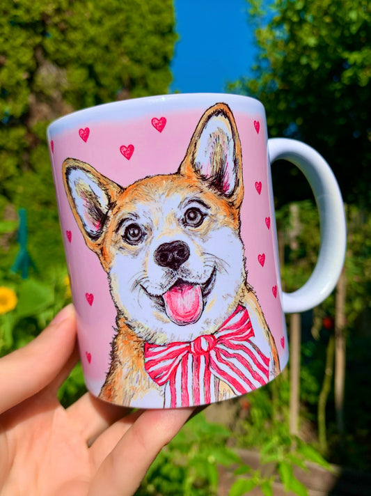 Kerámia bögre kézzel rajzolt, akvarellfestett világosbarna-fehér Corgi kutyával, ülő pózban és rózsaszín szív mintákkal, barátságos mosollyal, fehér háttérrel.