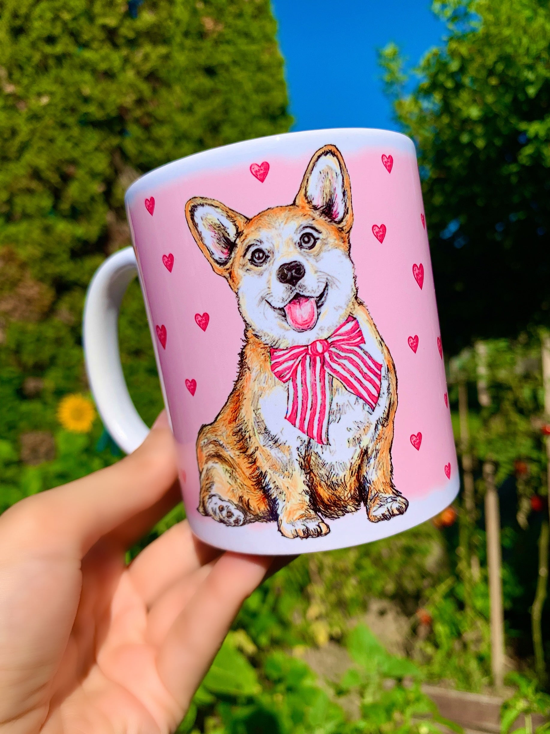Kerámia bögre világosbarna-fehér Corgi kutyával, kézzel rajzolt és akvarellfestett részletekkel, rózsaszín szív mintákkal, fehér háttérrel.