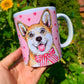 Kedves, mosolygó világosbarna-fehér Corgi illusztrációval díszített kerámia bögre, rózsaszín szív mintákkal és kézzel festett akvarell részletekkel.