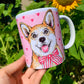 Kerámia bögre teljes alakos világosbarna-fehér Corgi kutya illusztrációval, rózsaszín szív mintákkal, részletes akvarell grafikával, fehér háttérrel.