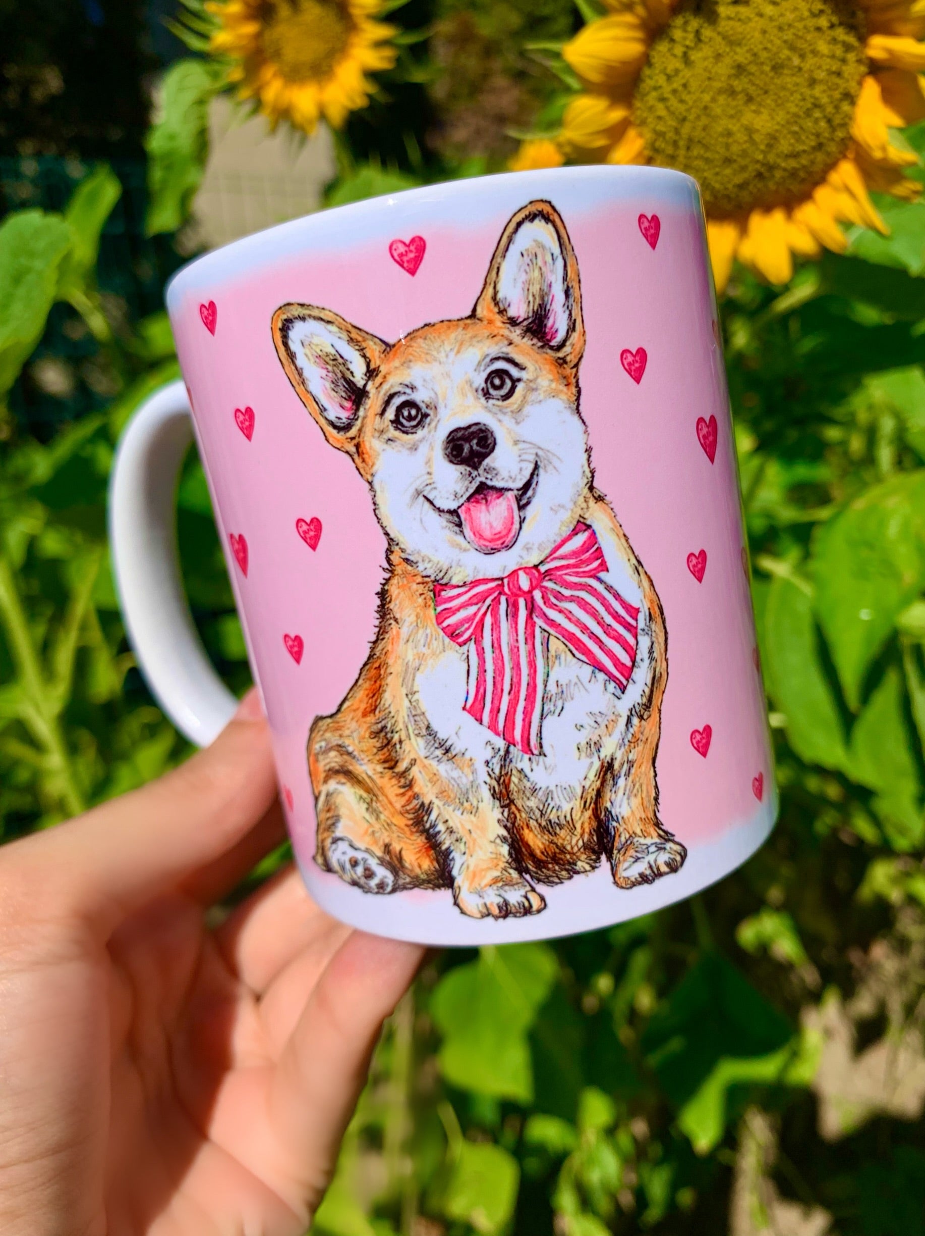 Kerámia bögre nagyított, kézzel festett világosbarna-fehér Corgi arcképpel, mosolygó tekintettel és rózsaszín szív mintákkal, fehér háttérrel.