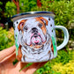 Ülő angol bulldog fém bögrén, fűben ülve, mancs mintás háttérrel