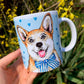 Kerámia bögre mosolygó Corgi kutyával és világoskék apró szív mintás háttérrel, kézzel rajzolt és festett részletekkel, fehér alapon.