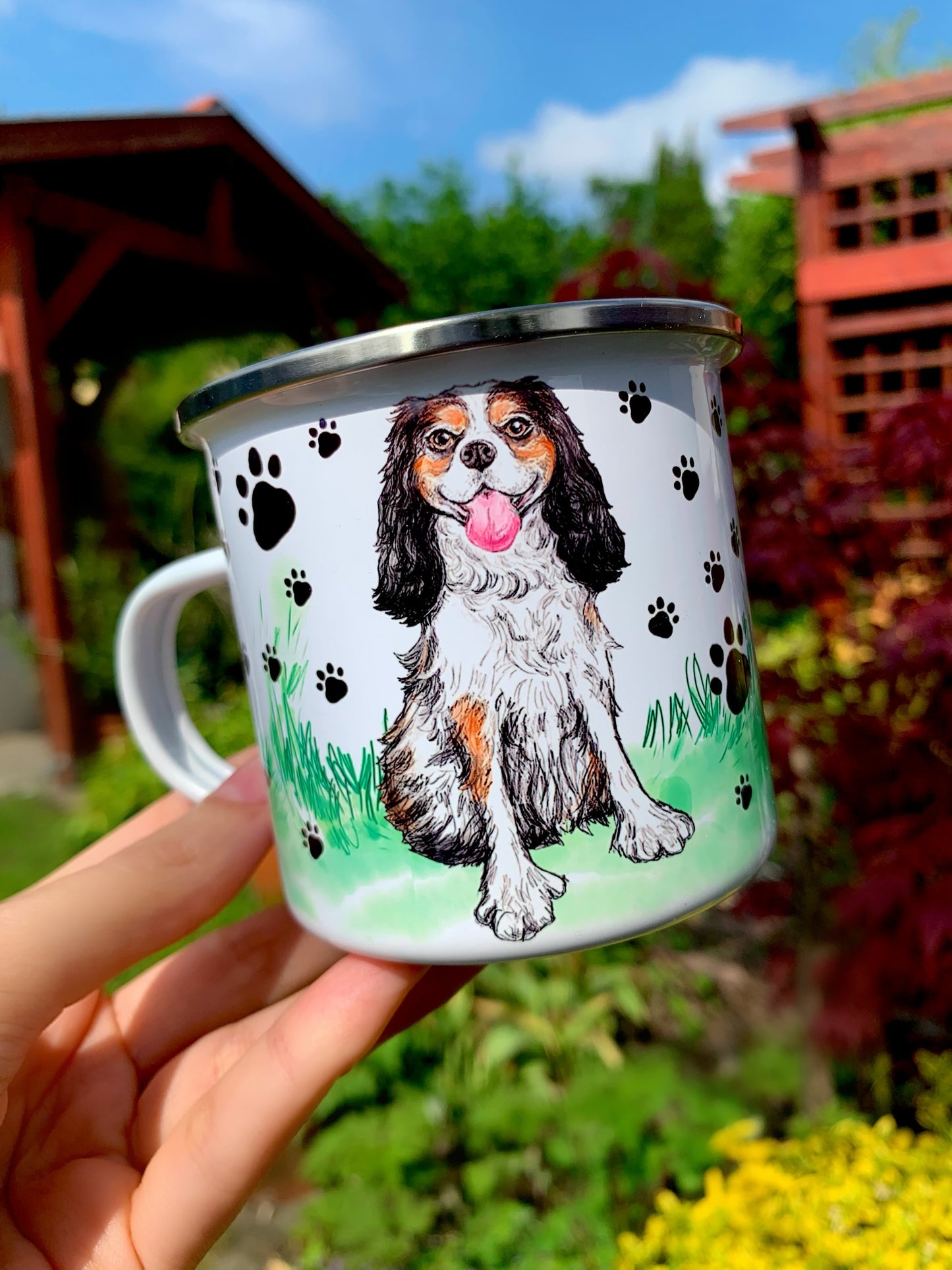 Mosolygó Cavalier spániel illusztráció fém bögrén, barna–fekete–fehér szőrzet, apró fekete mancs mintás fehér design, kézzel rajzolt és festett stílusban