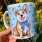 Mosolygó, világosbarna-fehér Corgi illusztrációval díszített kerámia bögre, kézzel festett világoskék apró szív mintákkal, fehér háttérrel.