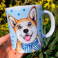 Kerámia bögre kézzel festett világosbarna-fehér Corgi kutyával és világoskék szív mintákkal, mosolygó kutyával, fehér háttérrel, részletgazdag grafikával. Prémium ajándék gazdiknak, kutyabarátoknak.