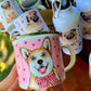 Romantikus stílusú fém bögre világosbarna-fehér Corgi kutyával, rózsaszín szív mintákkal és kézzel festett akvarell grafikával, fehér háttérrel.