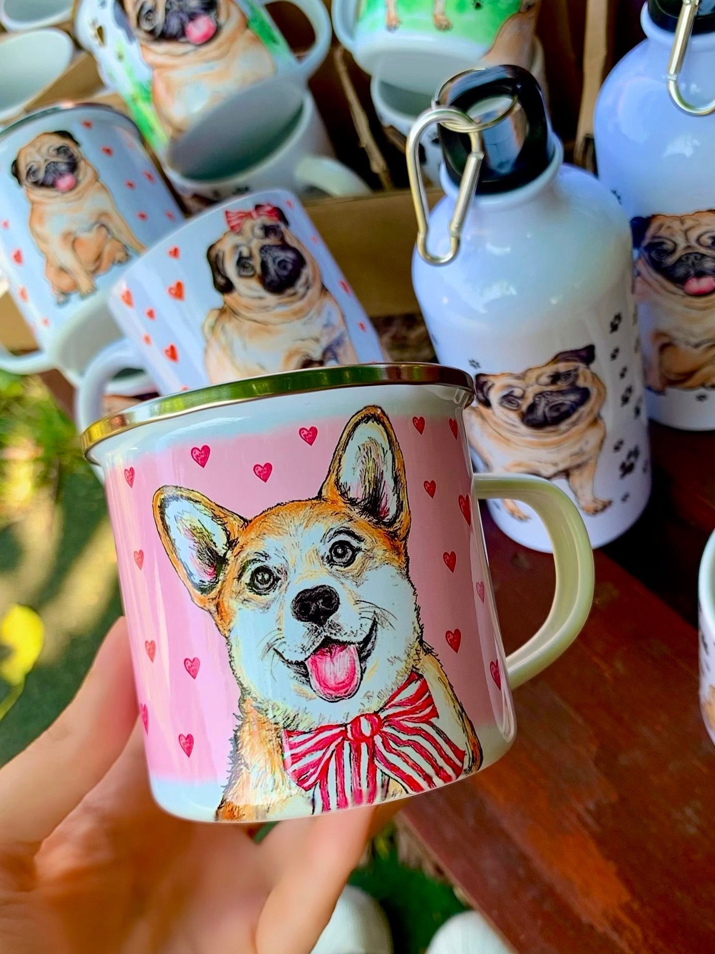Romantikus stílusú fém bögre világosbarna-fehér Corgi kutyával, rózsaszín szív mintákkal és kézzel festett akvarell grafikával, fehér háttérrel.