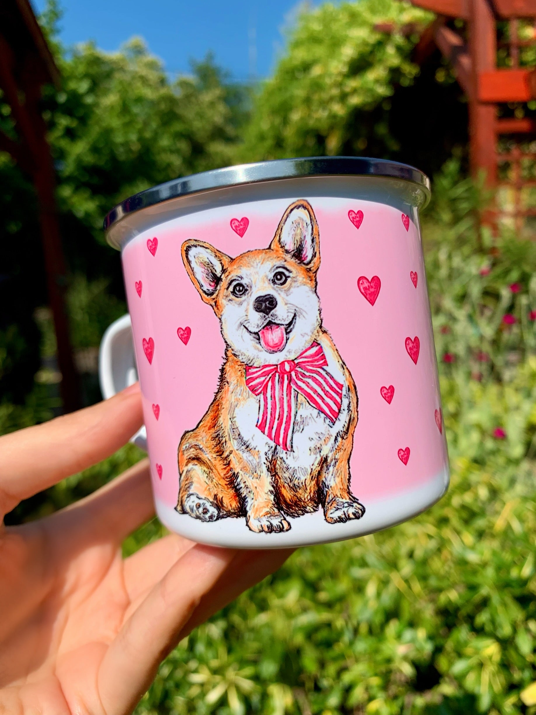 Fém bögre nagyított, kézzel festett világosbarna-fehér Corgi arcképpel, mosolygó tekintettel és rózsaszín szív mintákkal, fehér háttérrel.