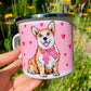 Közelkép a kézzel festett világosbarna-fehér Corgi arcáról fém bögrén, részletgazdag akvarell mintával és rózsaszín szívekkel, fehér háttérrel.
