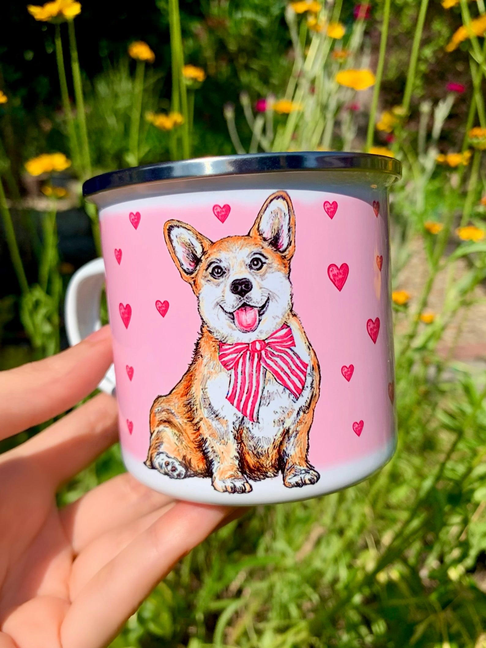 Közelkép a kézzel festett világosbarna-fehér Corgi arcáról fém bögrén, részletgazdag akvarell mintával és rózsaszín szívekkel, fehér háttérrel.