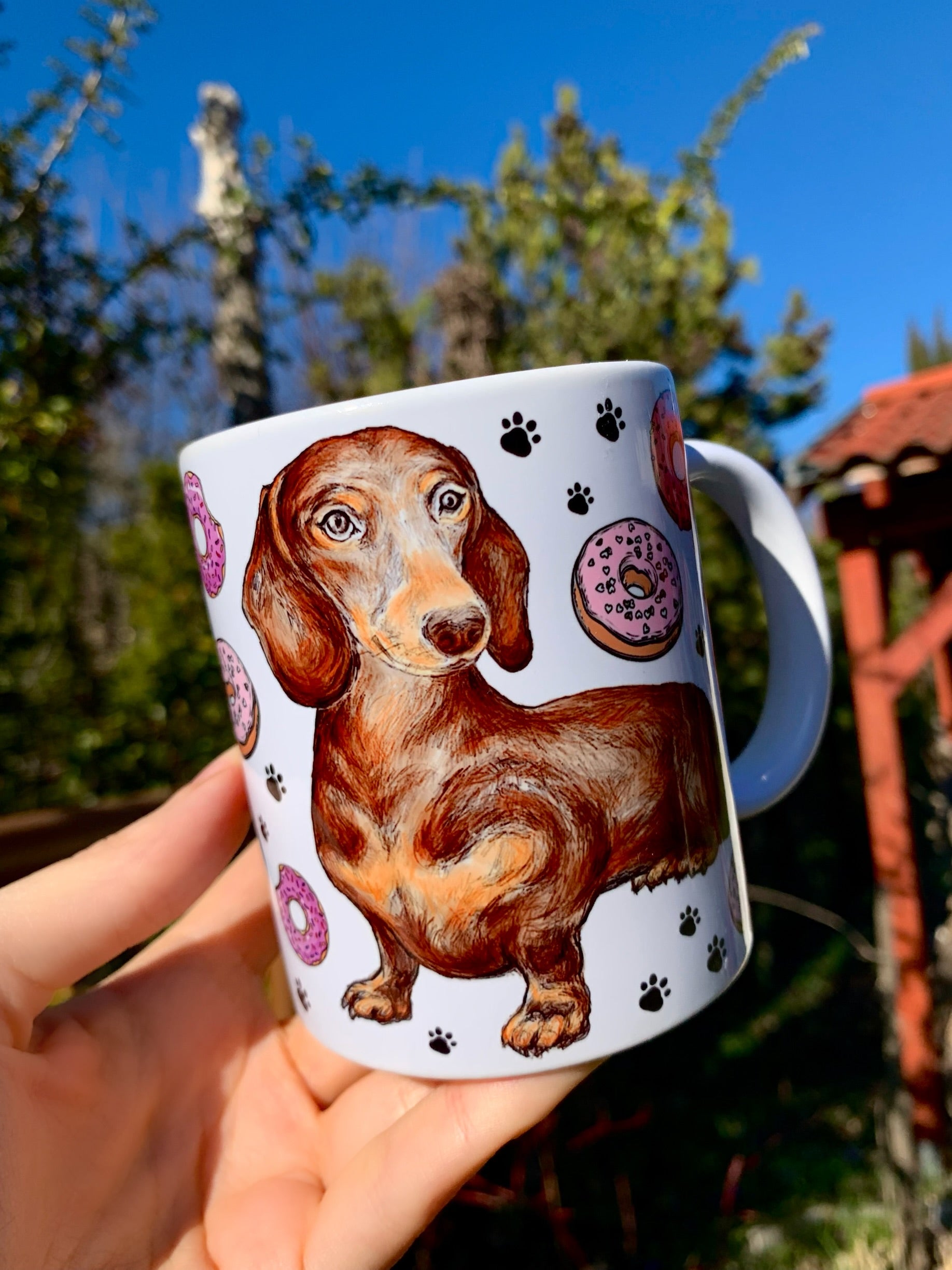 Részletgazdag akvarell csokibarna tacskó illusztráció, színes fánkokkal és apró fekete mancsokkal díszítve – kézzel festett kerámia bögrén.