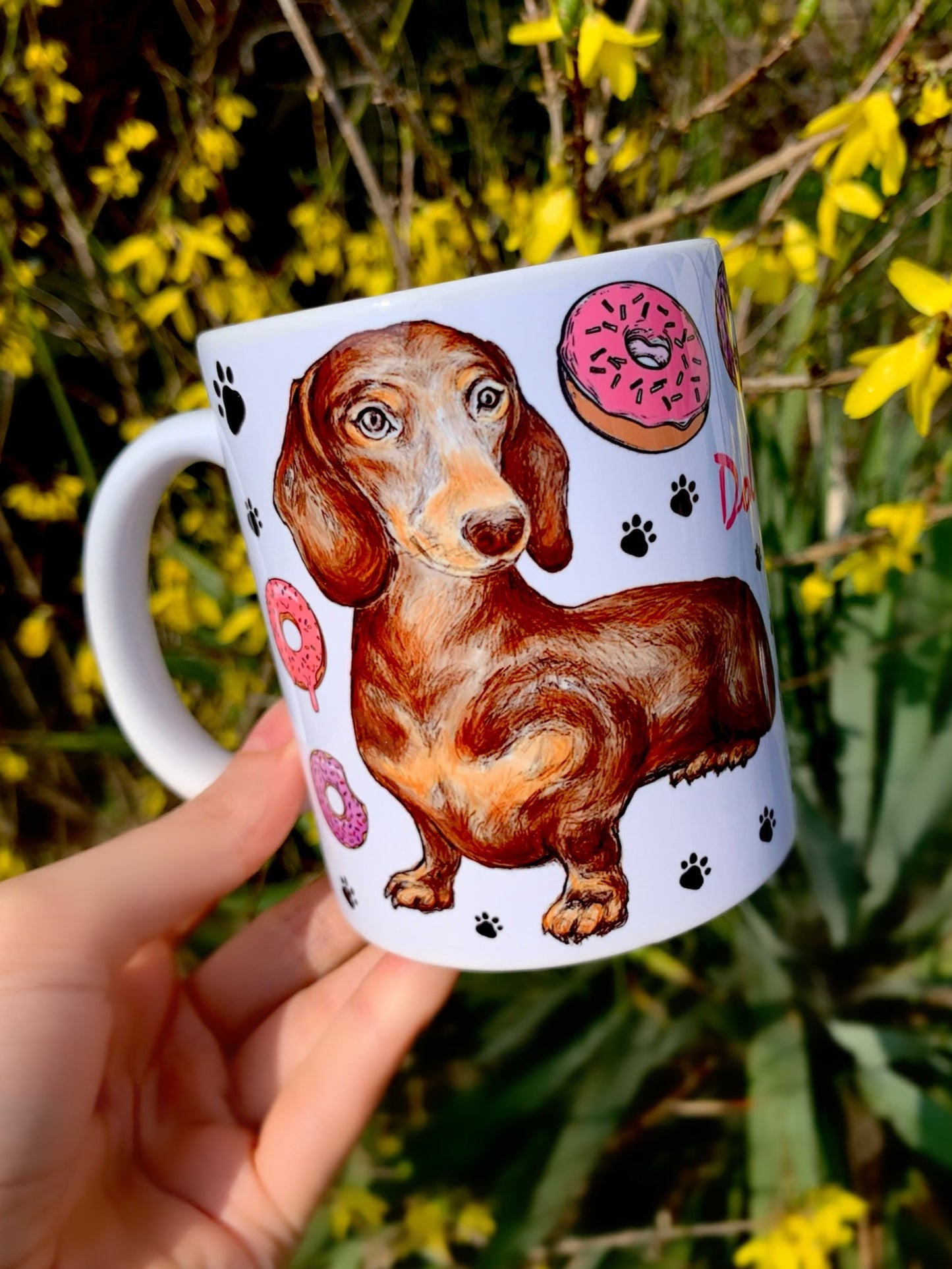 Vidám csokibarna tacskó, körülötte színes sütemények és apró fekete mancsnyomok – kézzel festett, prémium kerámia bögre tacskó rajongóknak.