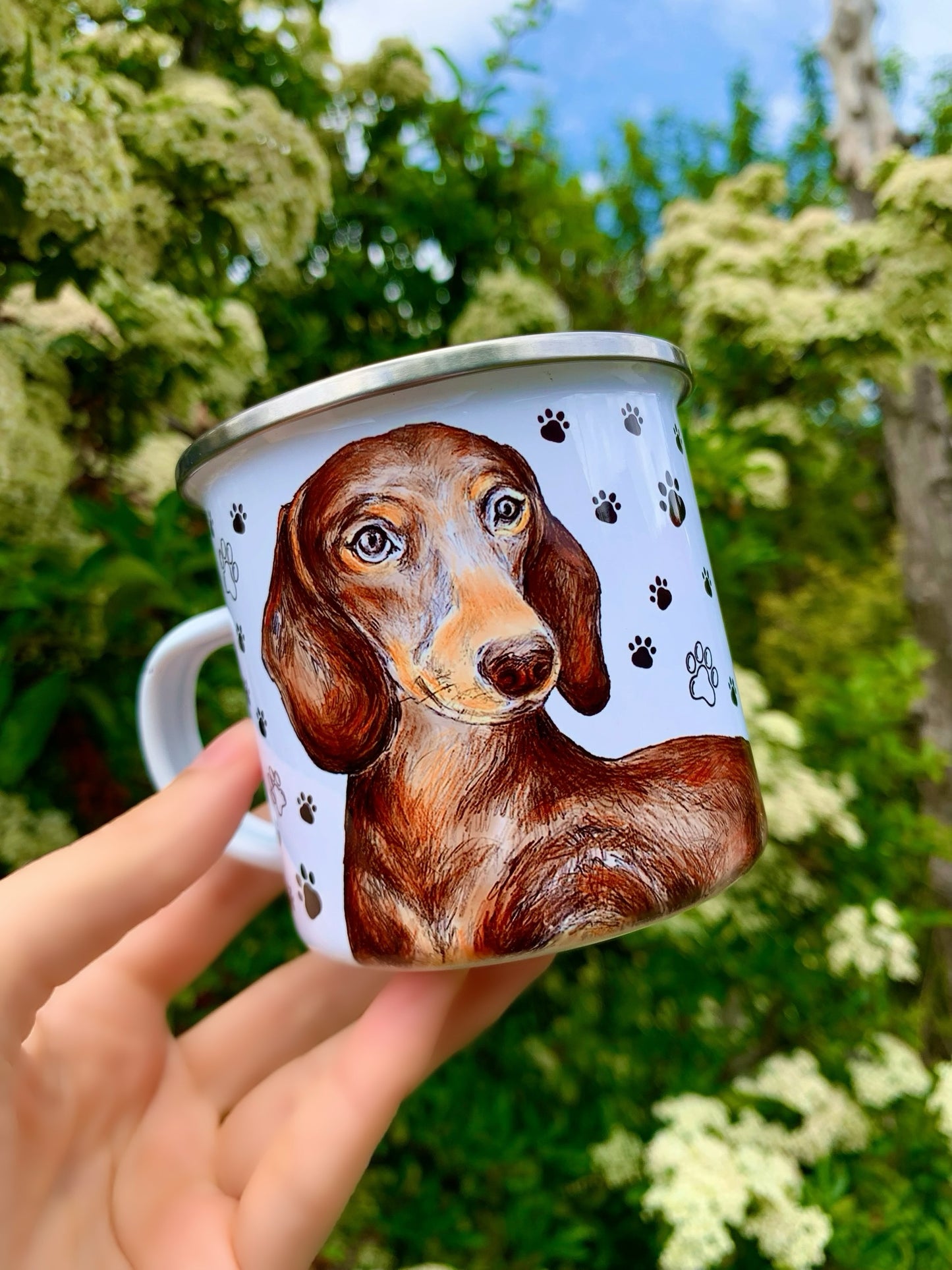 Chocolate tacskó portré akvarell stílusban, lágy ecsetvonásokkal és fényes bundaszínnel, játékos fekete mancsnyom mintával, tartós fém bögrén.