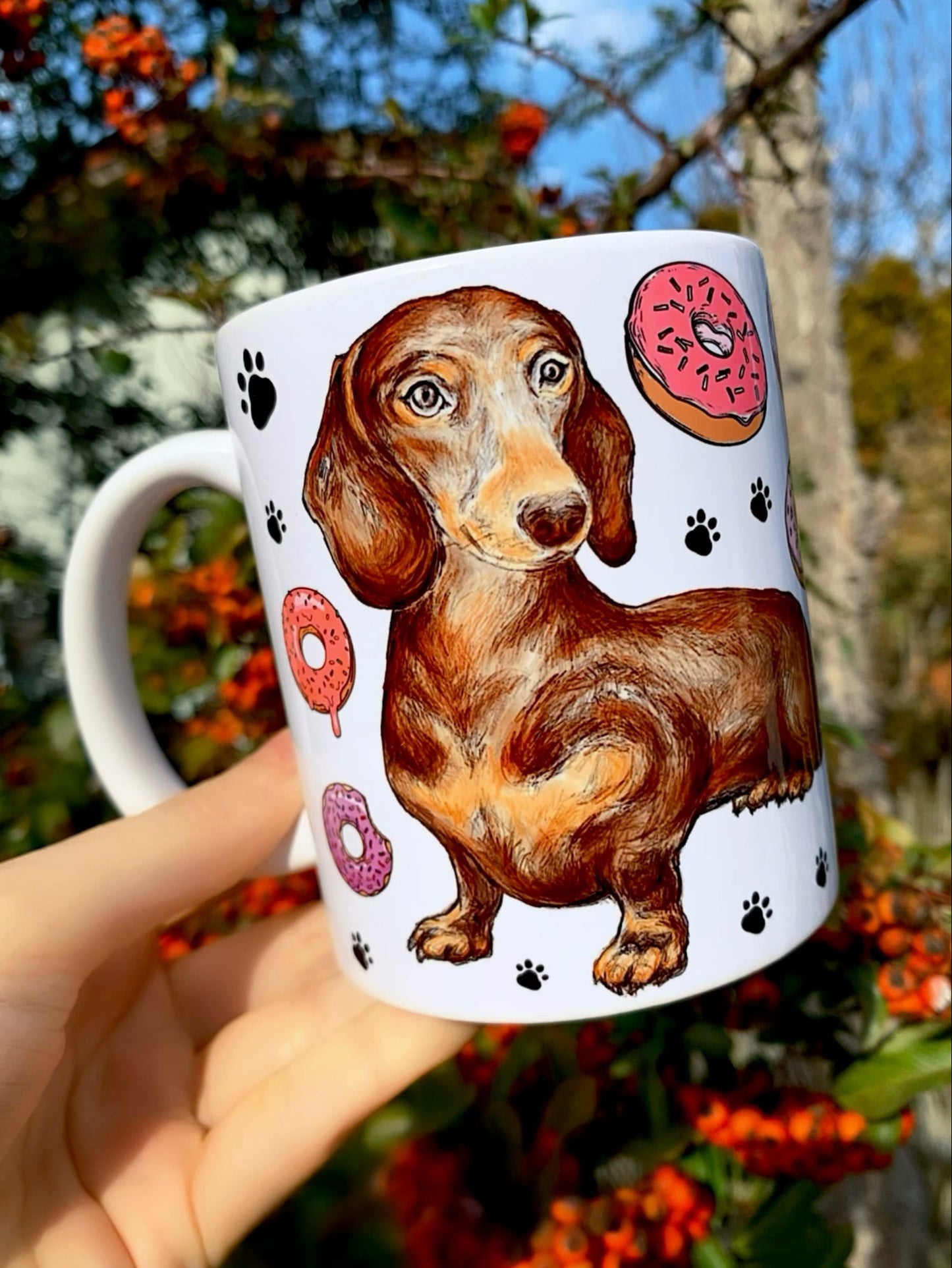 Prémium kerámia bögre kézzel festett csokibarna tacskóval, fánkokkal és fekete mancsnyomokkal – Pusztai Judit egyedi, akvarelles illusztrációja.