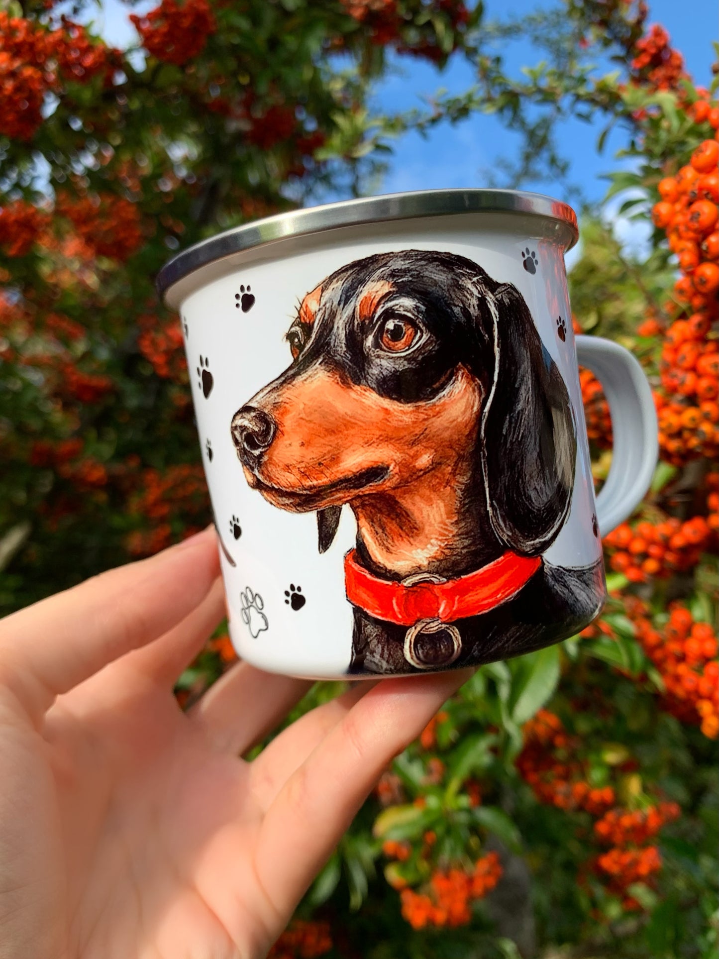 Akvarell festett cser tacskó portré és teljes alakos kutya minta fém bögrén, apró fekete mancs nyomokkal díszített háttérrel.