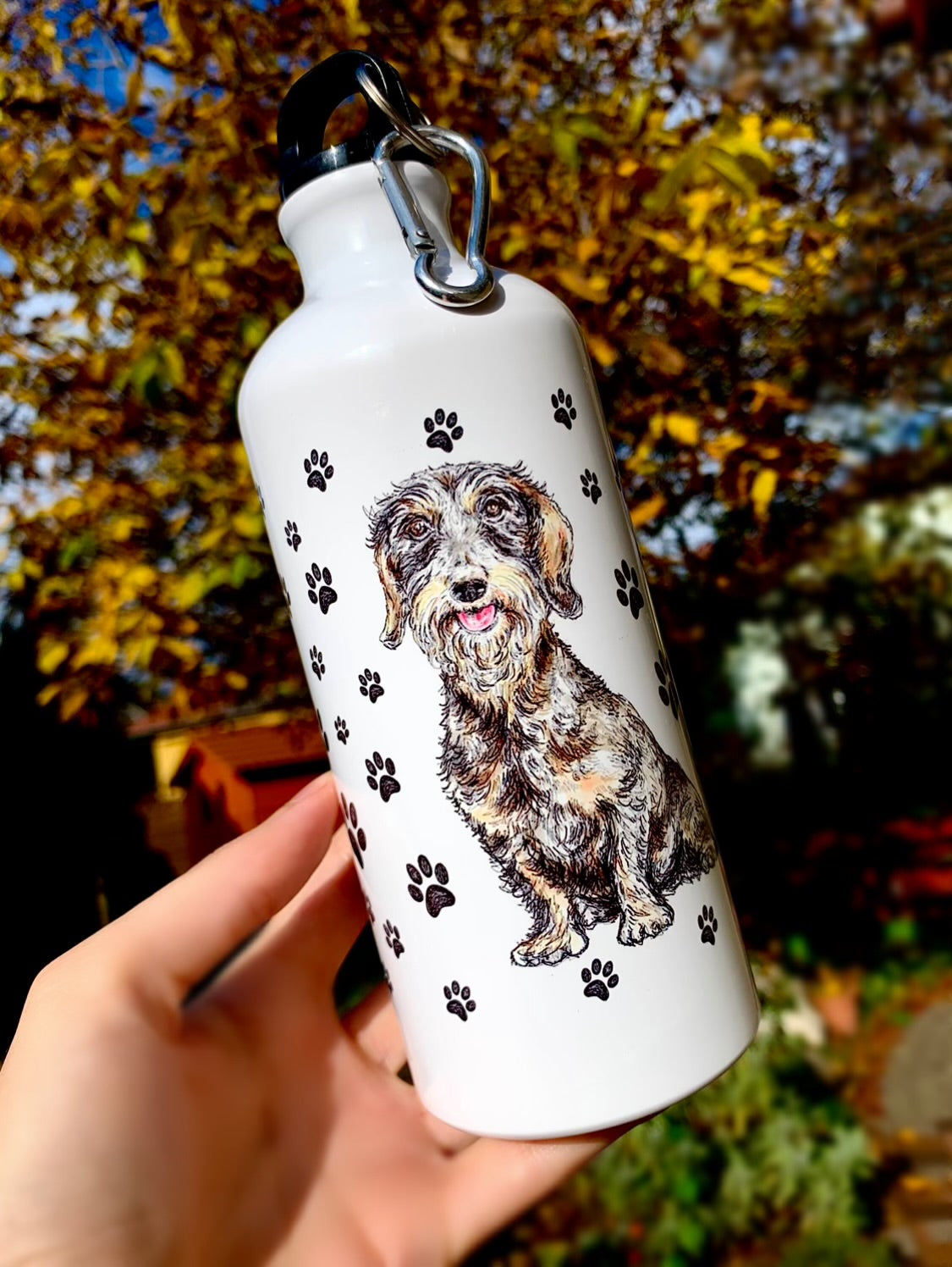 A kulacs különlegessége a kézzel festett szálkásszőrű tacskó grafika, amely minden részletében autentikus és szerethető. A könnyű fém alap tökéletes társ utazáshoz, sétákhoz és aktív életmódhoz. Tacskó gazdiknak készült, akik szeretnék magukkal vinni kedvencüket minden nap.